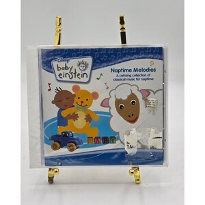 以下が含まれることがあります： 青と白のデザインのBaby Einstein CDケース。クマ、羊、青いトラックのイラストが特徴です。「Naptime Melodies」と「お昼寝のためのクラシック音楽の落ち着いたコレクション」と書かれています。