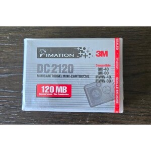 Op de afbeelding: Een verzegelde Imation DC2120 minicartridge met een rode strip. Het label toont de Imation- en 3M-logo's, evenals de tekst "120 MB". Compatibel met QIC-40, QIC-80, IRWIN-40 en IRWIN-80. De tekst "MINICARTRIDGE/MINI-CARTOUCHE" is ook zichtbaar.