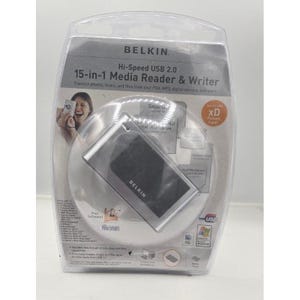 Peut inclure: Un lecteur et graveur de cartes multimédia 15-en-1 Belkin Hi-Speed USB 2.0 argenté et noir dans un emballage de vente au détail en plastique transparent. L'emballage présente du texte détaillant la compatibilité avec diverses cartes mémoire.