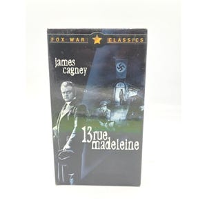 Puede incluir: Una caja de DVD de la película "13 Rue Madeleine" con James Cagney. La caja tiene un fondo oscuro con un efecto de foco, el título y el texto "FOX WAR CLASSICS". La portada incluye una bandera nazi.