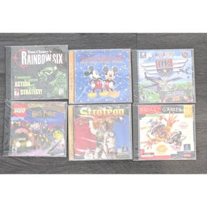 Op de afbeelding: Zes verzegelde pc-gamecases worden getoond. Titels zijn onder meer "Tom Clancy's Rainbow Six", "Mickey's Magical Christmas", "eGames RC Daredevil", "Lego Creator Harry Potter", "Strategy" en "Smart Games 3". De cases zijn van plastic.