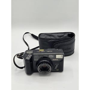 May include: Black Konica MR.70 camera with a black carrying case. The camera has a Konica lens and the text "MR.70" and "70" printed on the front. The camera strap is black.