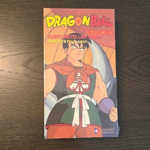 May include: A Dragon Ball VHS tape featuring the title "Fortune Teller Baba: Yamcha's Fall (Uncut)". The cover art showcases a character in a red and green outfit with a determined expression. The tape is in its original packaging.