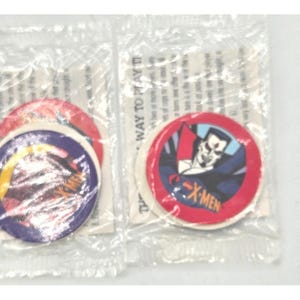Può includere: Due confezioni sigillate di pedine da gioco collezionabili degli X-Men. Ogni pezzo circolare presenta un'illustrazione di personaggio diversa con il logo X-Men. I pezzi sono rossi, blu e gialli.
