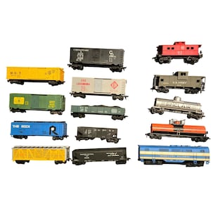May include: A selection of model railway carriages in diverse colours, such as yellow, green, blue, and black. Each carriage displays unique markings and designs, representing different railway companies and carriage types. The image shows a variety of freight carriages and a caboose.