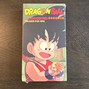 May include: A Dragon Ball VHS tape featuring a cartoon image of a young boy holding a dragon ball. The tape has the title "Dragon Ball" in yellow and red, with the text "Commander Red" and "Danger for Hire". The packaging is sealed in plastic.