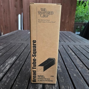 May include: A rectangular cardboard box for a Pampered Chef Bread Tube-Square, item number 1555. The tan packaging features black text and a graphic illustration of the square-shaped metal baking tube inside, with the product name printed vertically.
