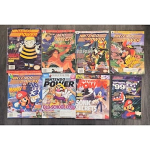 May include: A collection of eight vintage Nintendo Power magazines featuring various video game characters on the covers, including Mario, Sonic, Banjo-Kazooie, and Tarzan. Each issue displays the iconic Nintendo Power logo and colourful graphics.