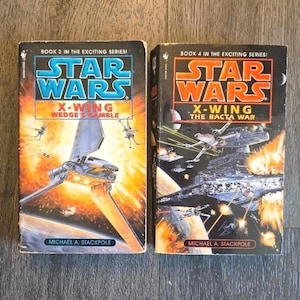 Puede incluir: Dos novelas vintage de Star Wars X-Wing. El libro 2, "Wedge's Gamble", presenta una ilustración de una nave espacial con un fondo naranja y azul. El libro 4, "The Bacta War", muestra una escena de batalla espacial. Ambos libros son de Michael A. Stackpole.
