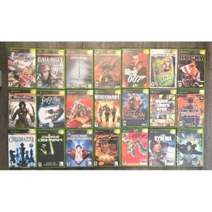 May include: A collection of twenty-one Xbox video game cases arranged in three rows of seven. The titles include Call of Duty, Star Wars Jedi Knight, Halo 2, 007 From Russia With Love, Oddworld Munch's Oddysee, Rocky, Prince of Persia, and others.