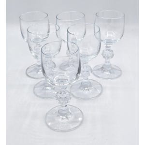 Puede incluir: Seis copas de vino transparentes con tallo decorativo y cuenco redondo. Las copas son de cristal transparente y tienen una base circular. Los tallos presentan un diseño esférico. Están dispuestas sobre una superficie blanca.