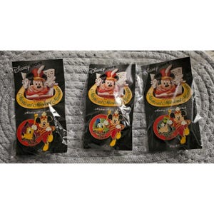 Könnte beinhalten: Drei Disney Store Pins mit Mickey Mouse in einem rot-goldenen Outfit, mit dem Text "Magical Musical Moments". Jeder Pin hat ein kreisförmiges Design mit Mickey Mouse und anderen Charakteren. Die Pins befinden sich auf schwarzen Rückenkarten.