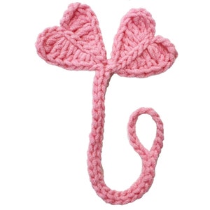 May include: Pink crocheted bookmark with two heart-shaped wings and a long tail.