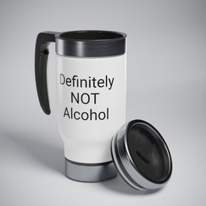 May include: A white travel mug with a black lid and handle. The mug has a silver band around the top and bottom. The text "Definitely NOT Alcohol" is printed on the mug.