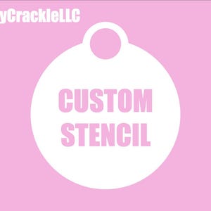 May include: A white, circular stencil design with the words "CUSTOM STENCIL" in pink, set against a light pink background. The text "CraftyCrackleLLC" is in white at the top left. The stencil has a small loop at the top.