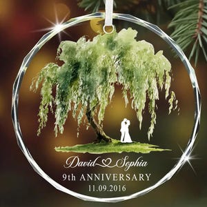 Op de afbeelding: Een heldere, ronde glazen ornament met een aquarel schilderij van een treurwilg. Silhouetten van een stel staan onder de boom. De tekst luidt "David & Sophia 9th ANNIVERSARY 11.09.2016".