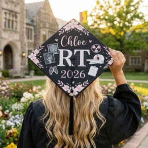 Könnte beinhalten: Schwarze Abschlusskappe mit rosa floralen Akzenten und dem Namen "Chloe" in Schreibschrift. Die Kappe zeigt medizinische Bildgebungssymbole, die Buchstaben "RT" und das Jahr "2026". Eine schwarze Quaste hängt von der Kappe.