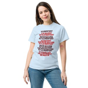 Peut inclure: Un t-shirt bleu clair avec un motif de texte rouge et noir qui dit "ILS MENTENT ILS SAVENT QU'ILS MENTENT NOUS SAVONS QU'ILS MENTENT ILS SAVENT QUE NOUS SAVONS QU'ILS MENTENT NOUS SAVONS QU'ILS SAVENT QUE NOUS SAVONS QU'ILS MENTENT ET POURTANT ILS CONTINUENT DE MENTIR"