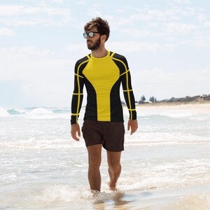 May include: A black long-sleeved shirt with yellow geometric designs. The shirt is worn by a person standing on a beach.