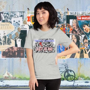 Puede incluir: Una camiseta gris con un gráfico de temática de los Beatles. El gráfico presenta un collage de signos de interrogación y las palabras "There will be an answer" y "Let it be".