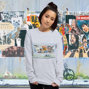 May include: A grey long-sleeved shirt featuring a graphic print of a street scene with a motorcycle and graffiti. The graphic is a collage of vintage Beatles album covers.