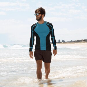 May include: A man wearing a black and blue long-sleeved shirt with geometric patterns. He is standing on a beach.