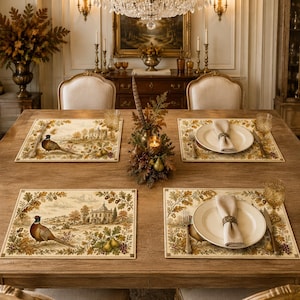 May include: A dining table set with four rectangular placemats featuring a printed scene of a pheasant, a country house, and oak leaves. Each setting includes a white ceramic plate, a folded beige napkin with a ring, and a silver fork and knife.