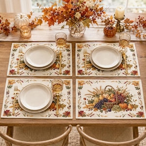 Peut inclure: Un ensemble de quatre sets de table rectangulaires en tissu avec un motif sur le thème de la récolte, incluant des feuilles d'automne, du blé et un panier en osier rempli de fruits et légumes, bordés de feuillages colorés.
