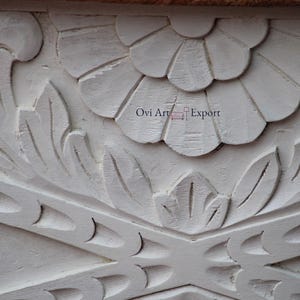 Peut inclure: Sculpture florale en bois blanc avec des d&eacute;tails complexes. La sculpture pr&eacute;sente une grande fleur au centre et de plus petits motifs floraux autour. Le bois est peint en blanc et a une finition lisse.
