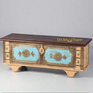 May include: A wooden storage chest with two doors, painted in a light cream color with blue accents and gold metal details. The top of the chest is made of dark wood.