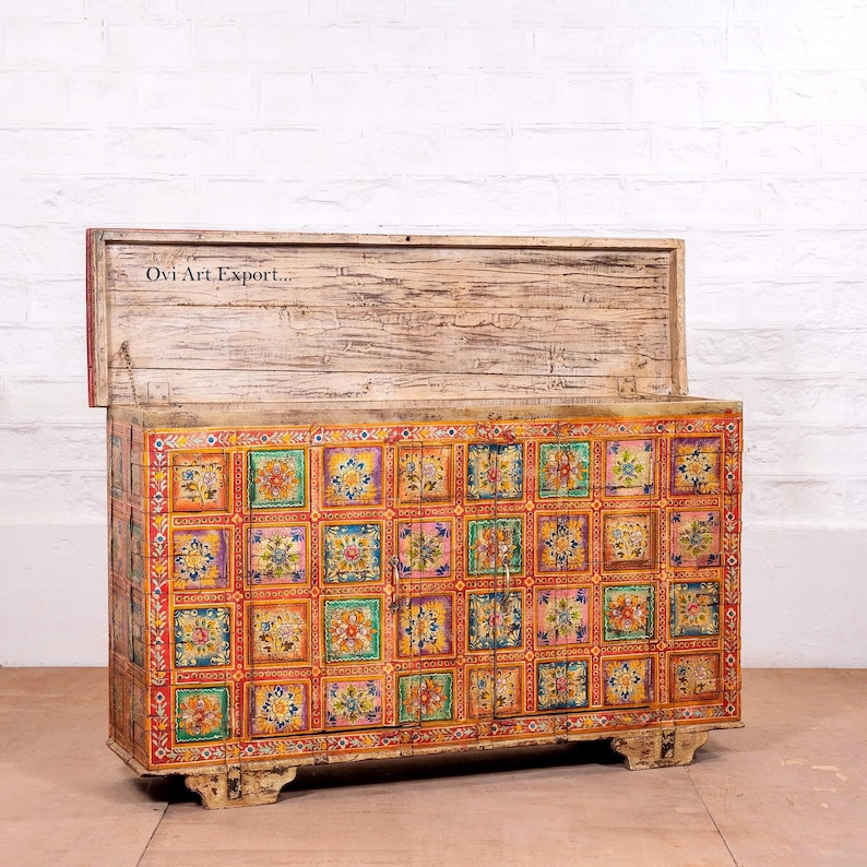 Puede incluir: Un cofre de madera con tapa con bisagras, pintado con un colorido patr&oacute;n de baldosas florales. El cofre es rectangular con un acabado blanco envejecido en la tapa y la base. El texto "Ovi Art Export..." es visible.