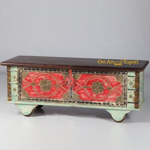 May include: A wooden storage chest with a distressed turquoise finish and intricate red and gold painted designs. The chest has a dark wood top and sits on four small wheels.