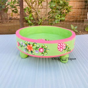 May include: A green wooden tray with pink trim and floral designs. The tray has three legs and is perfect for serving snacks or displaying decorative items.