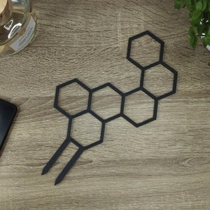 Op de afbeelding: Zwart metalen honingraatontwerp met een lange steel. Het honingraatontwerp bestaat uit zes aan elkaar verbonden zeshoeken.