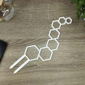 Op de afbeelding: Witte, honingraatvormige wanddecoratie van metaal. De decoratie heeft de vorm van een lange, gebogen lijn.