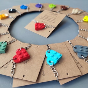 Op de afbeelding: Een verzameling hartvormige bedelarmbanden in verschillende kleuren, waaronder rood, geel, groen en blauw. Elke bedel is verbonden met een zilveren ketting en wordt gepresenteerd op een bruine kaart. De armbanden zijn in een cirkelvorm gerangschikt.