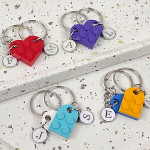 Op de afbeelding: Vier sets sleutelhangers met hartvormige LEGO-steenbedels in rood, paars, blauw en geel. Elke sleutelhanger heeft een zilveren letterbedel.