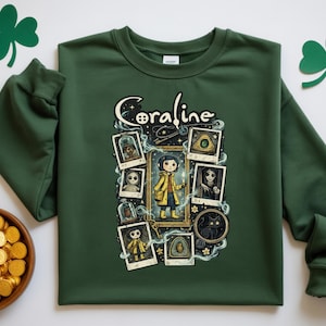 Op de afbeelding: Een bosgroene sweater met ronde hals en een grafische print met de tekst Coraline. Het ontwerp bevat een centrale illustratie van een personage in een gele regenjas, omringd door diverse ingelijste polaroid-stijl afbeeldingen en magische rook.