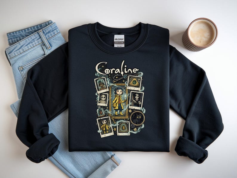 Op de afbeelding: Een zwart sweatshirt met ronde hals en een grafische print met de tekst Coraline. Het ontwerp bevat een centrale illustratie van een personage in een gele regenjas, omringd door verschillende ingelijste polaroid-stijl afbeeldingen van figuren.