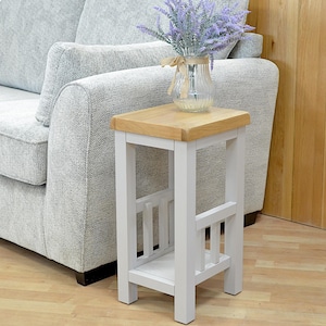 May include: A white side table with a wooden top and a shelf. The table has a simple design with vertical slats on the sides. A vase with purple flowers sits on top of the table.