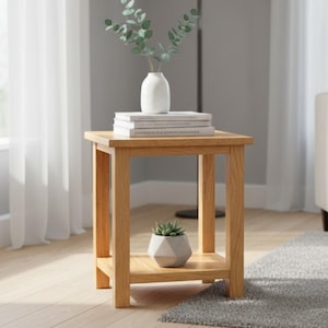 May include: A light oak square side table with a lower shelf. A white vase with greenery and books sit on top. A small geometric planter with a succulent is on the lower shelf. The table is 51 cm tall.