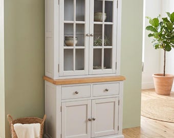 May include: A light gray wooden hutch cabinet featuring a natural wood top surface. The upper section has two glass-paneled doors with small round knobs, while the lower base includes two drawers and two solid cabinet doors with matching hardware.