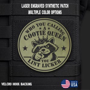 May include: A circular olive green laser engraved synthetic patch featuring a raccoon wearing a crown and pointing forward. The text reads: WHO YOU CALLING A COOTIE QUEEN YOU LINT LICKER. The patch has a hook backing and is attached to black webbing.