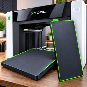 May include: An xTool laser machine with a white and black exterior featuring the green xTool logo. Two rectangular black plates with bright green edges are positioned in front of the machine, one lying flat and one standing vertically.