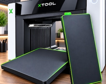 May include: An xTool laser machine with a white and black exterior featuring the green xTool logo. Two rectangular black plates with bright green edges are positioned in front of the machine, one lying flat and one standing vertically.