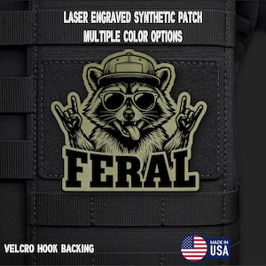 May include: A laser engraved synthetic patch with a Velcro hook backing featuring a raccoon wearing a baseball cap and sunglasses, making a rock and roll hand gesture with both paws. The text FERAL is printed below the raccoon graphic.