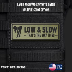 May include: A rectangular olive green laser engraved synthetic patch with a black silhouette of a person bending over and the text LOW & SLOW - THAT'S THE WAY TO GO. The patch features a hook backing and is attached to a black tactical gear surface.
