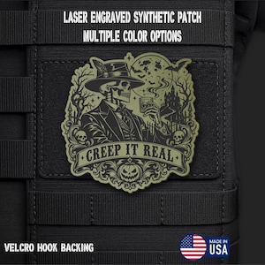 May include: A laser engraved olive green synthetic patch with a Velcro hook backing. The design features a skeleton in a suit and hat holding a glass, with a haunted house, bats, and the text "CREEP IT REAL" above a carved pumpkin.