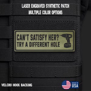 May include: A rectangular olive green synthetic patch with a black border and black text that reads CAN'T SATISFY HER? TRY A DIFFERENT HOLE, accompanied by a graphic of a power drill. The patch features a hook backing and is attached to black webbing.