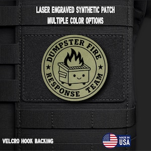 May include: A circular olive green synthetic patch with a laser-engraved dumpster fire graphic and the text DUMPSTER FIRE RESPONSE TEAM. The patch features a hook backing and is attached to a black tactical gear surface with MOLLE webbing.